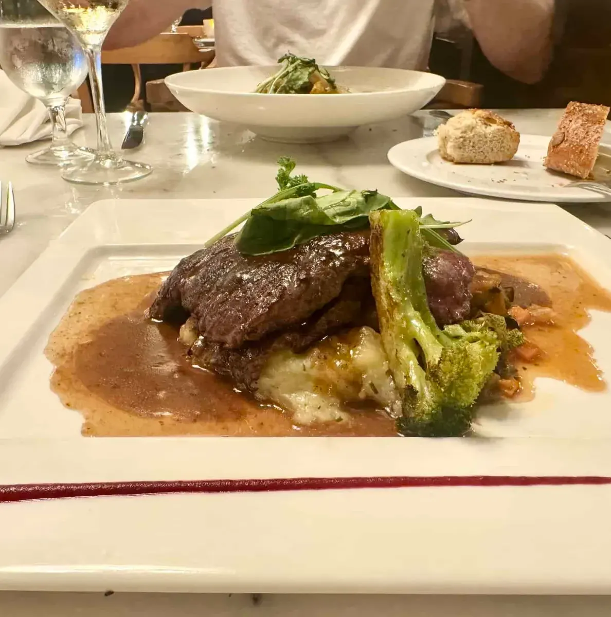 Succulent steak with vegetables and gravy served on a white plate at a fancy restaurant.