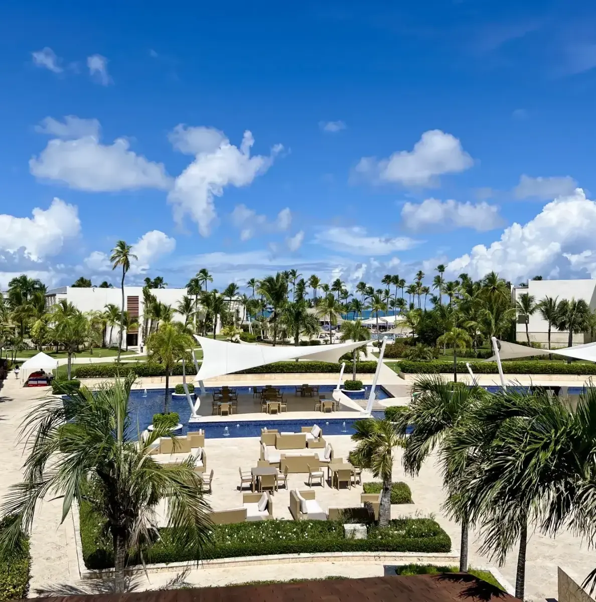 Pool area with palm trees, lounge chairs, and white shade structures