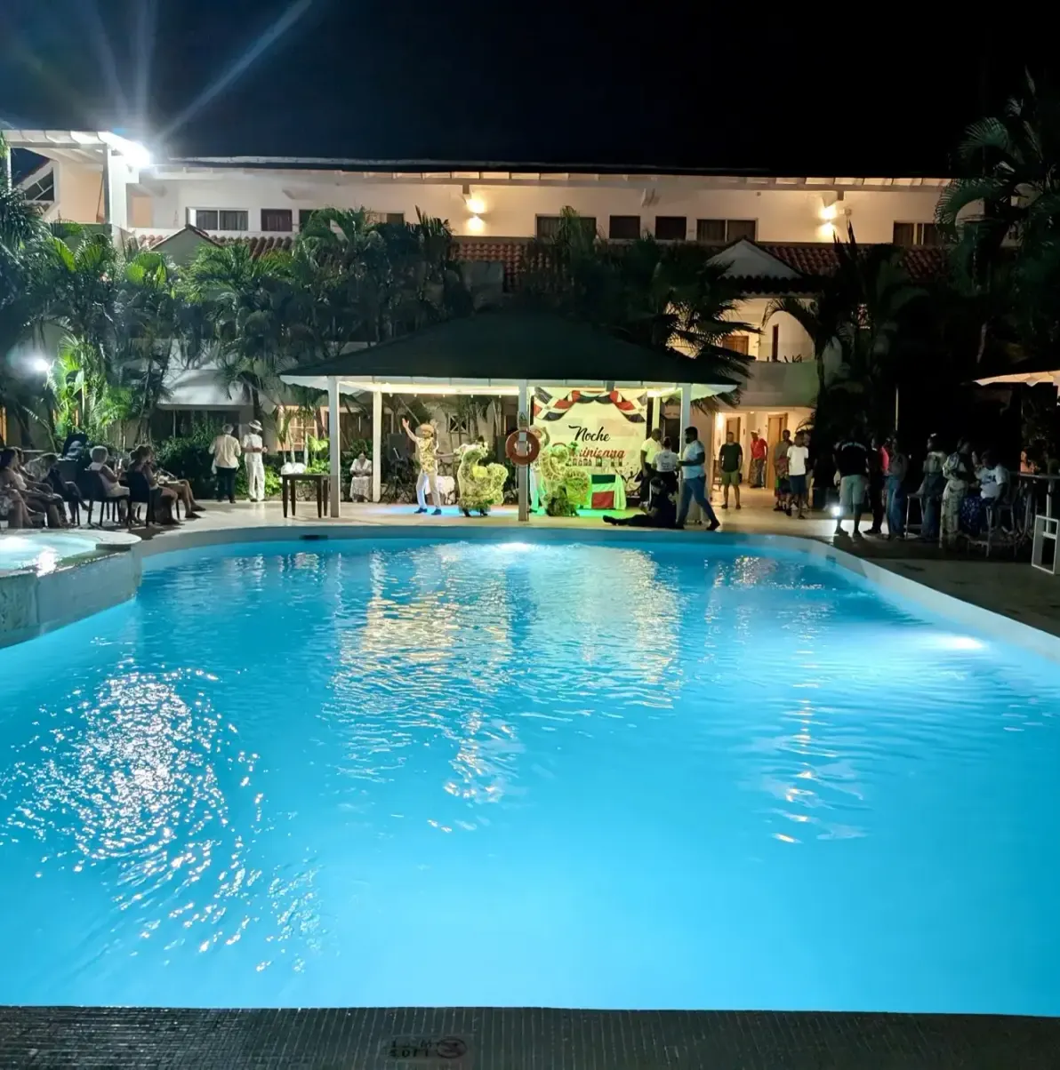 Pool at night with people around a covered stage area