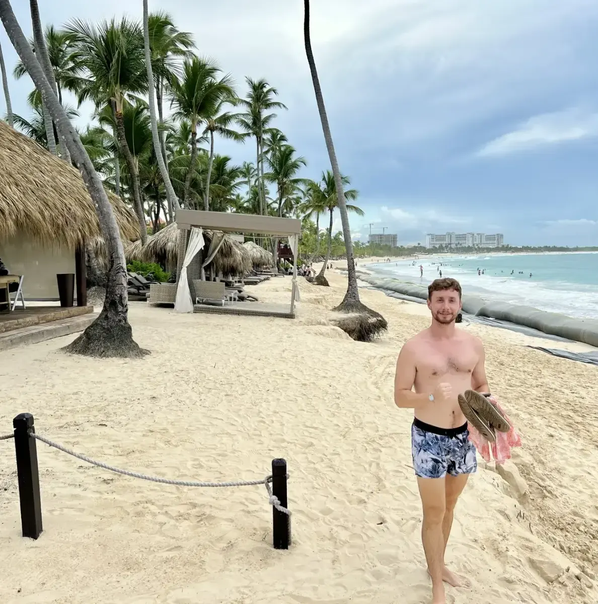 Man on sandy beach with palm trees, thatched structures, and ocean