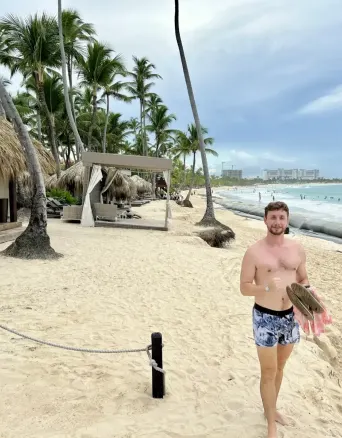 Man on sandy beach with palm trees, thatched structures, and ocean