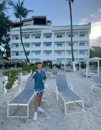Man standing on sandy beach with lounge chairs and a white building