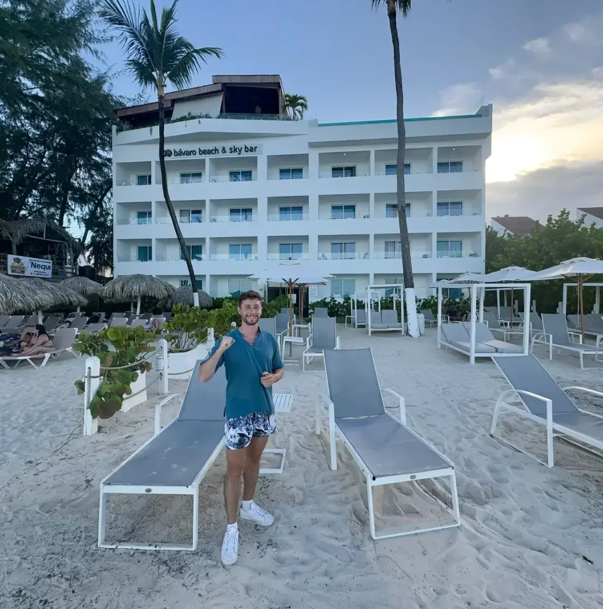 Man standing on sandy beach with lounge chairs and a white building