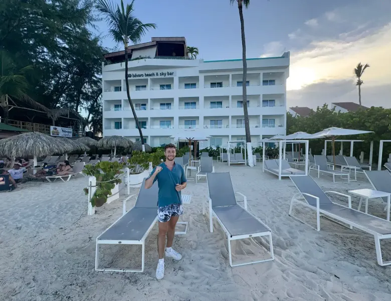 Man standing on sandy beach with lounge chairs and a white building