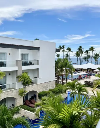 Balcony view of resort buildings, pool, palm trees, and beach