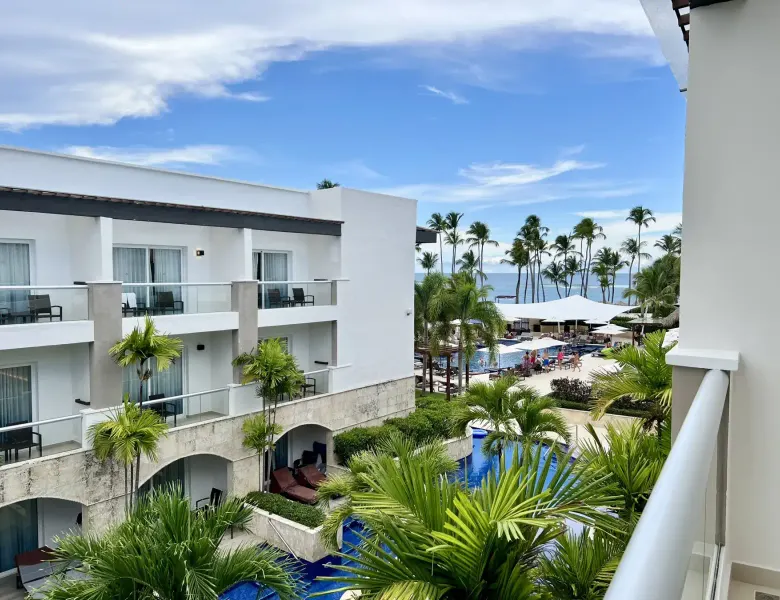 Balcony view of resort buildings, pool, palm trees, and beach