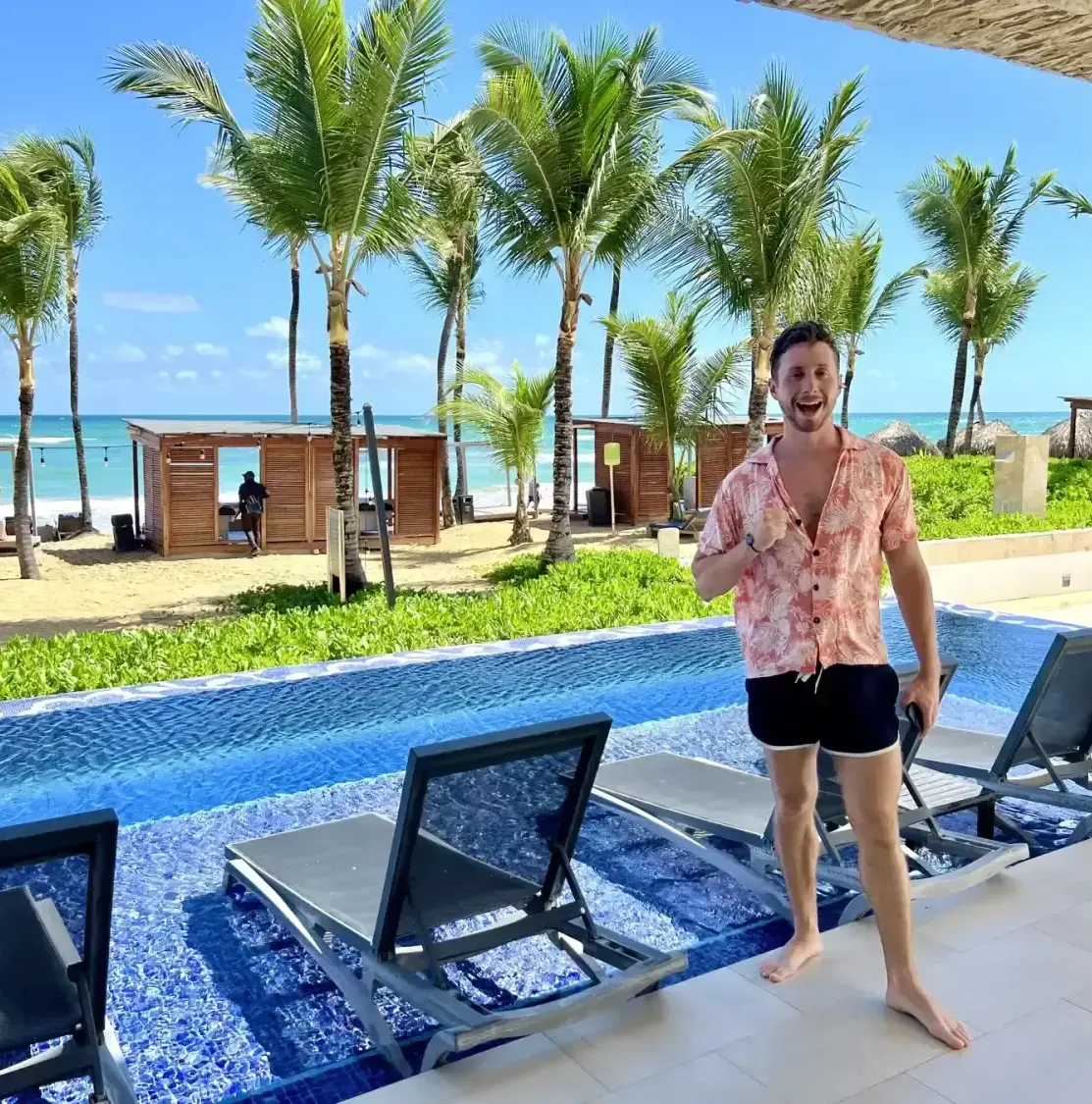 Man standing by pool with beach and palm trees in background