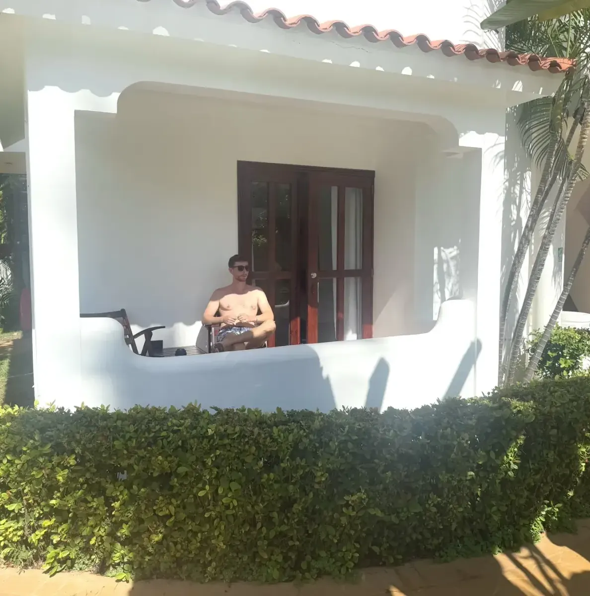 Man sitting on balcony of white building with red roof and green
