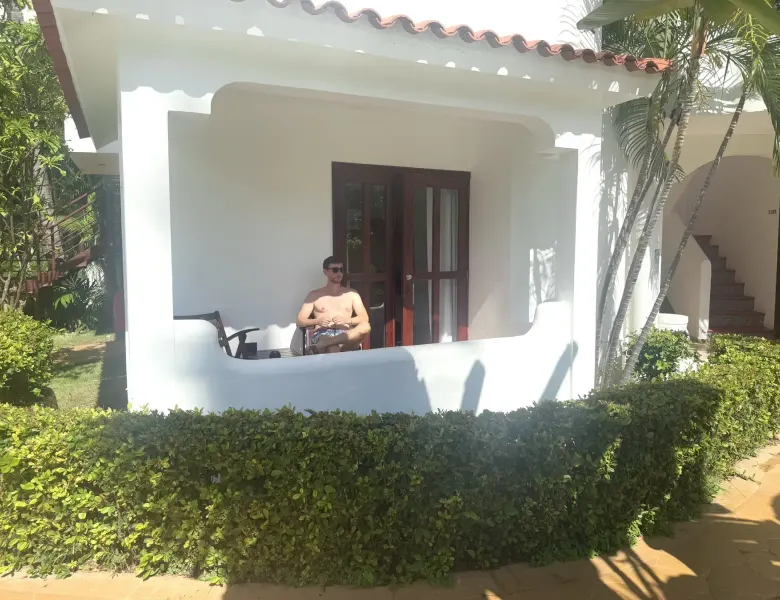Man sitting on balcony of white building with red roof and green