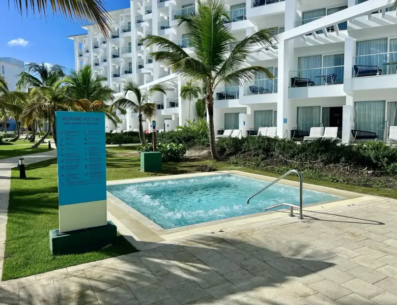 Jacuzzi with sign, palm trees, hotel building, lounge chairs, paved area