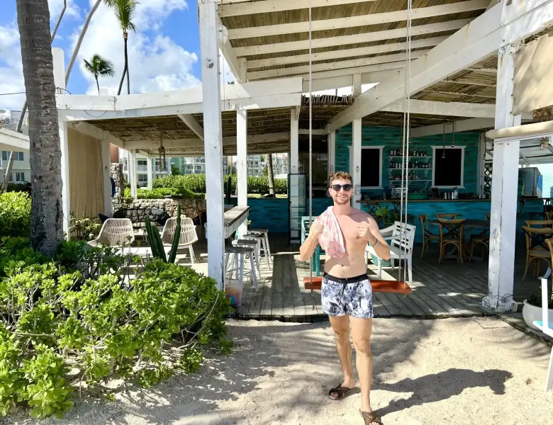 Man in swim trunks stands on sand near a bar