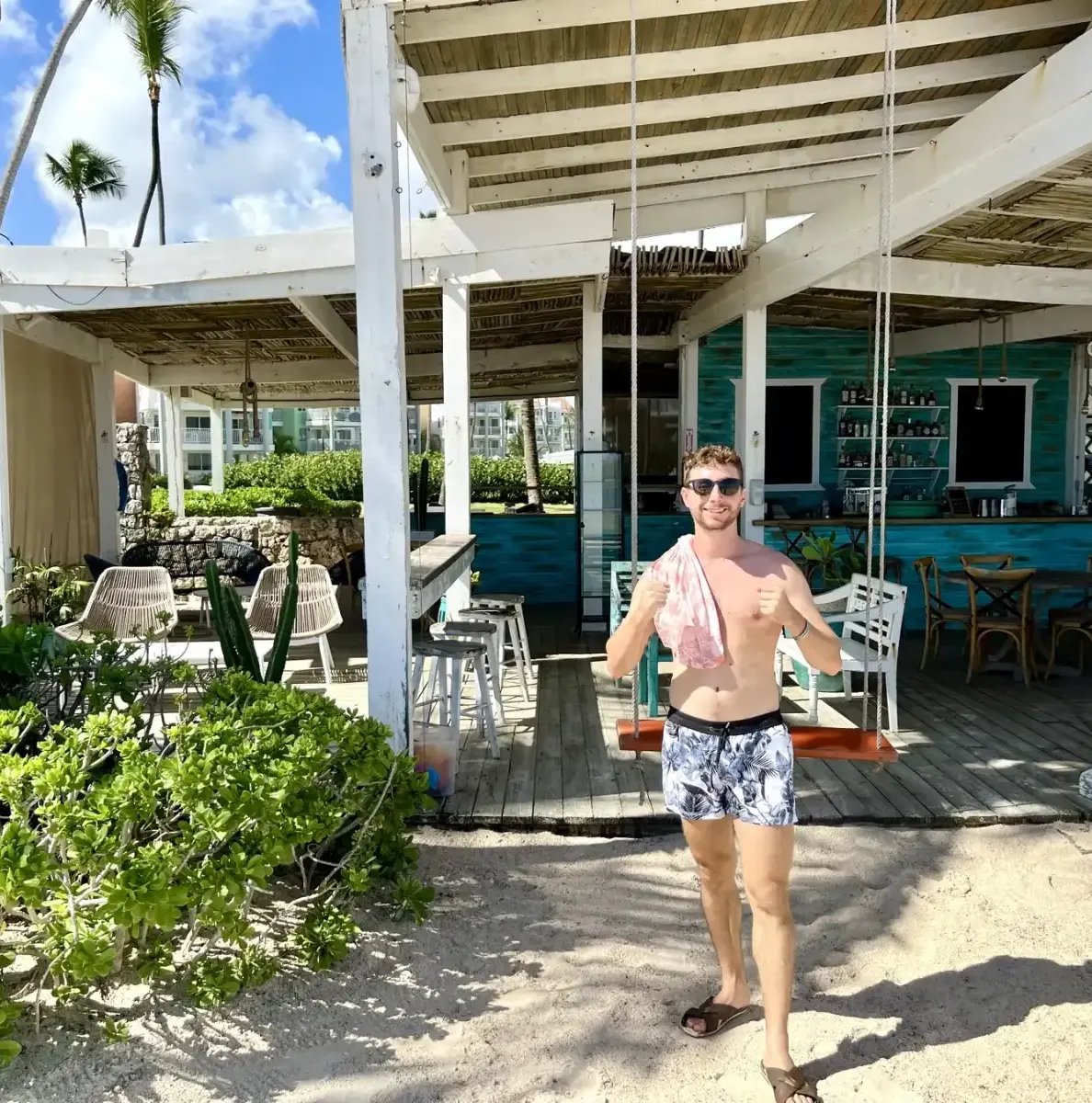 Man in swim trunks stands on sand near a bar