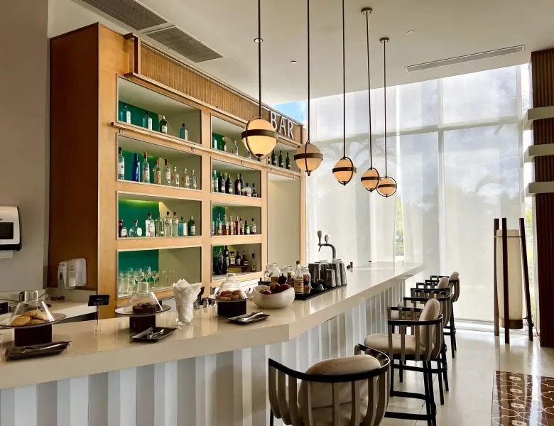 bar counter with stools, shelves of bottles, hanging lights, large windows