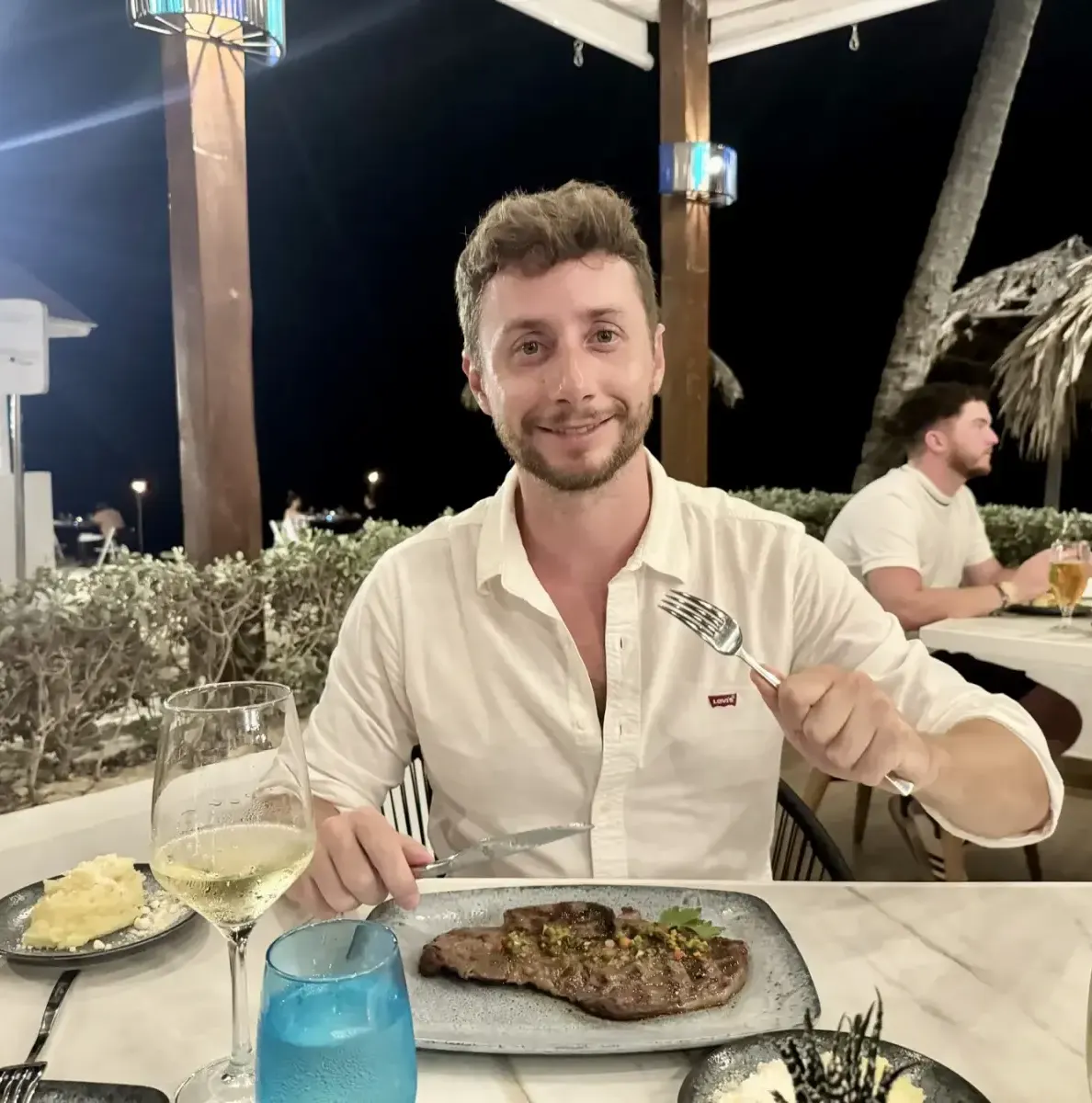 Man with fork and knife at table with steak, wine, and other