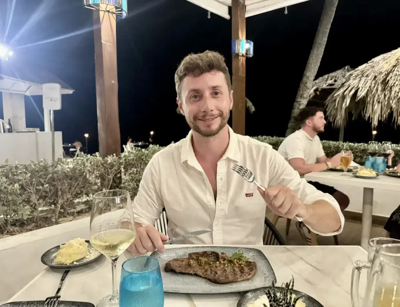 Man with fork and knife at table with steak, wine, and other