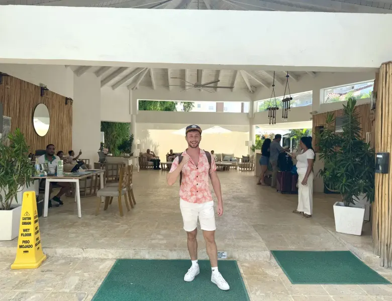 Man in pink shirt standing in resort lobby with people in background