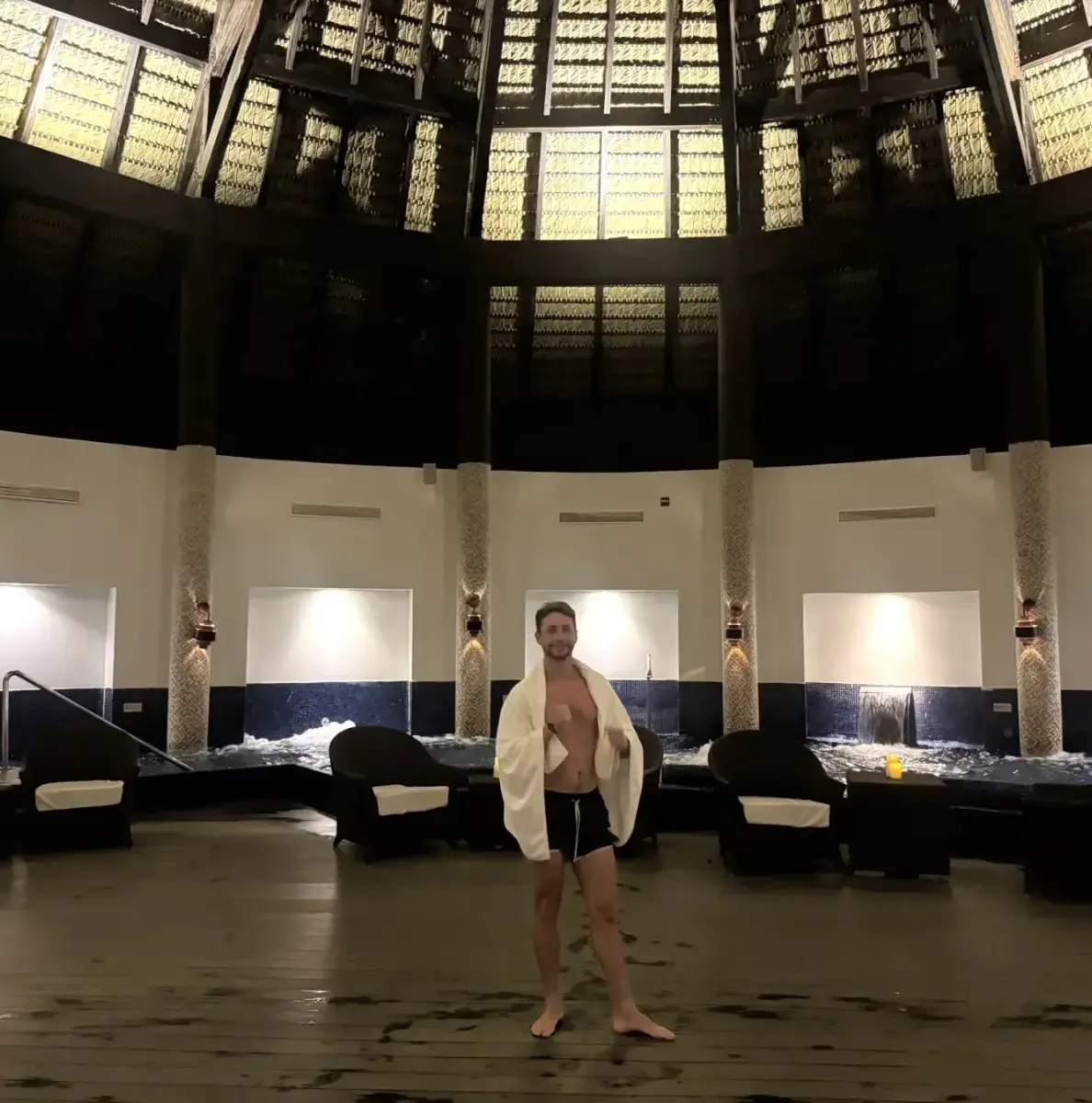 Man in towel and swim trunks stands in spa with jacuzzi pools