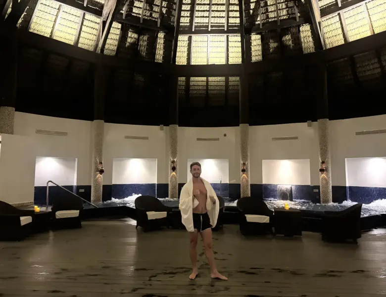 Man in towel and swim trunks stands in spa with jacuzzi pools