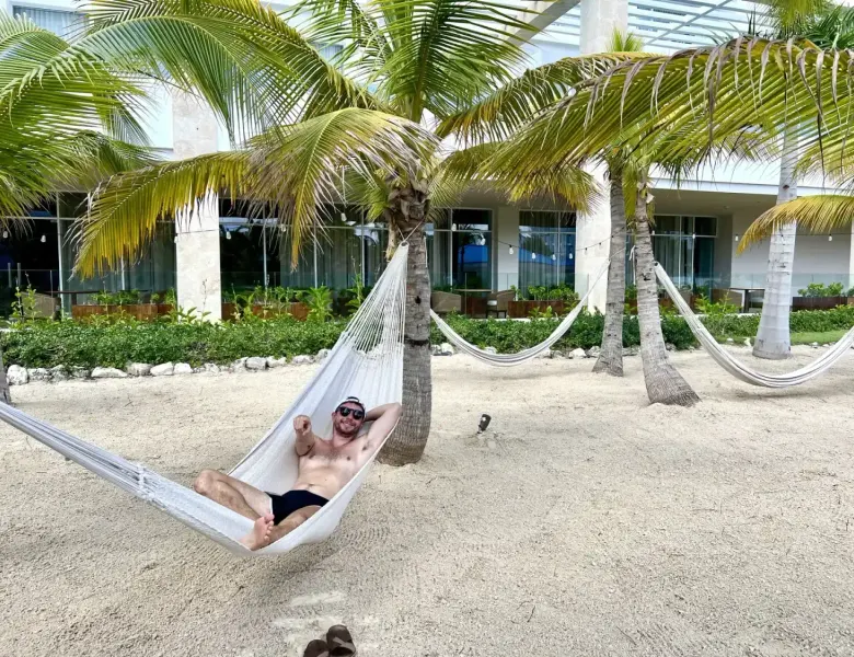 Man in hammock on sandy area with palm trees and resort building