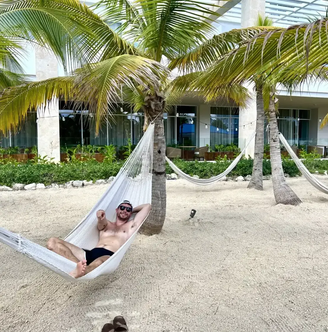 Man in hammock on sandy area with palm trees and resort building