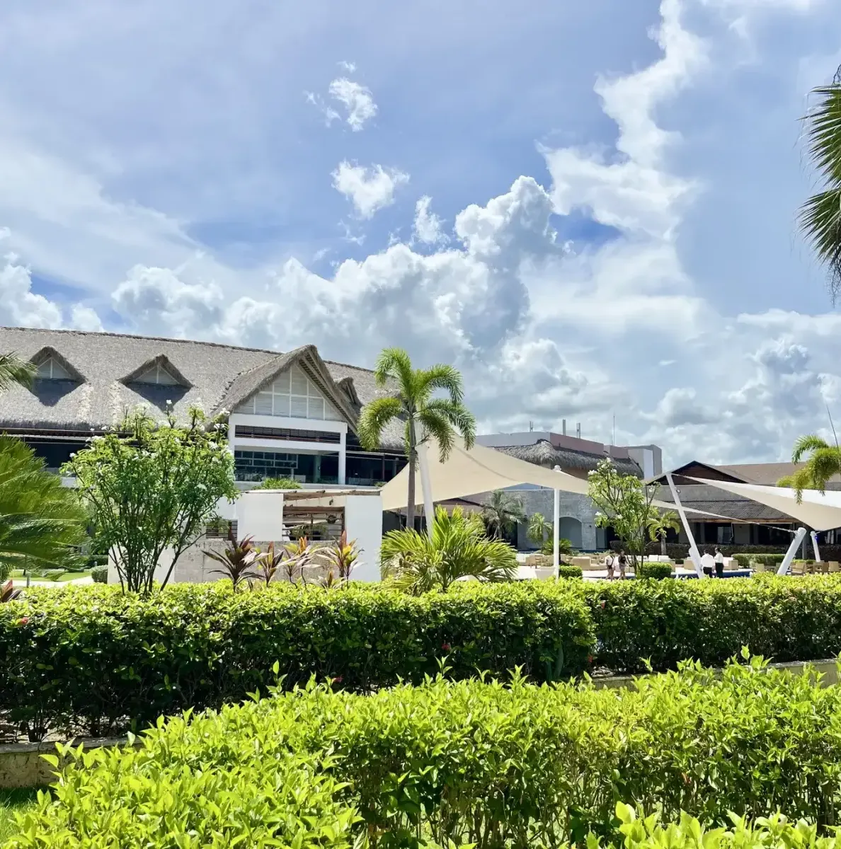 resort buildings, hedges, palm trees, white canopy, cloudy sky