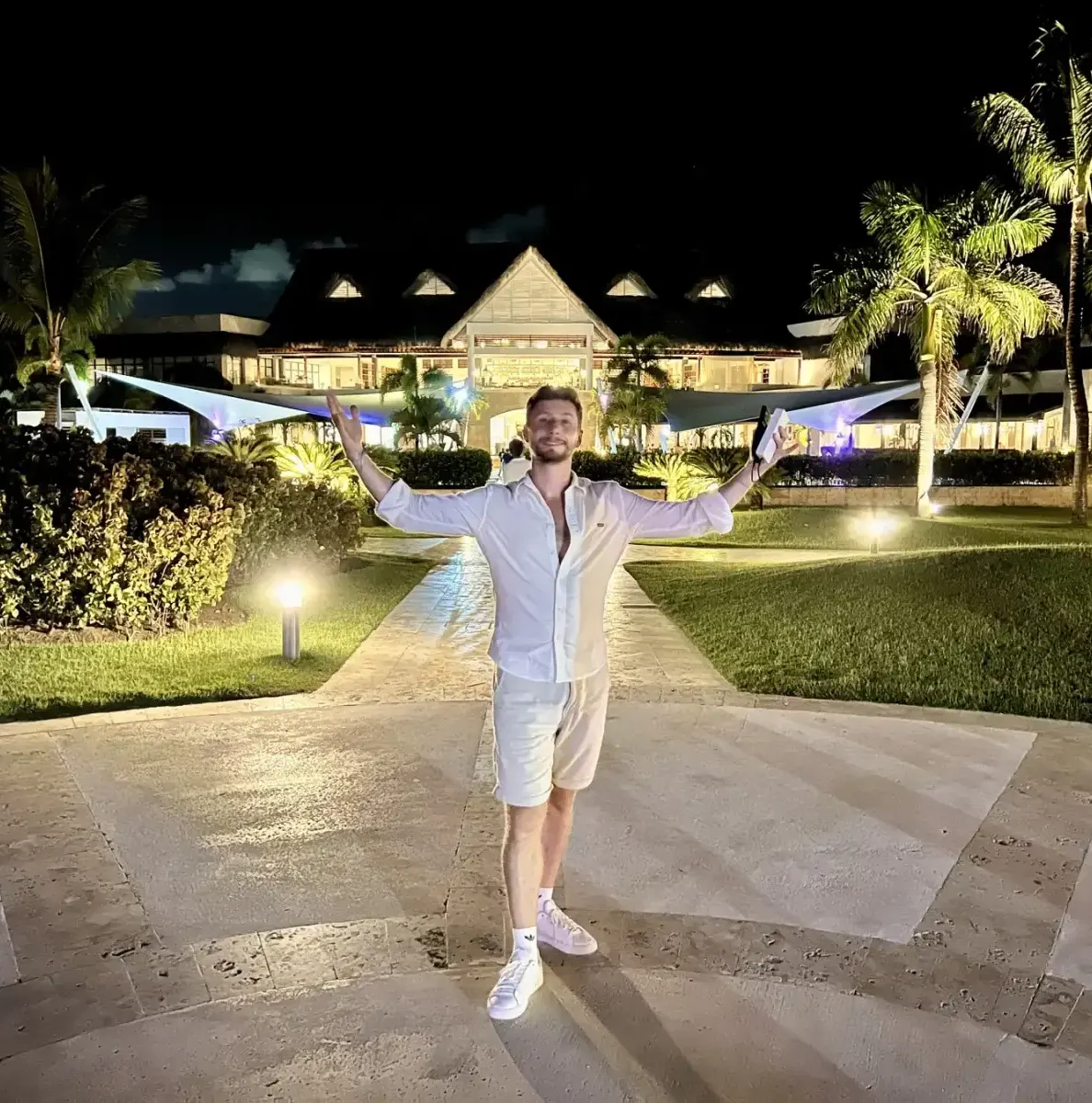 Man standing on path in front of lit building with palm trees