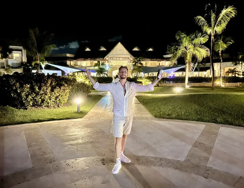 Man standing on path in front of lit building with palm trees