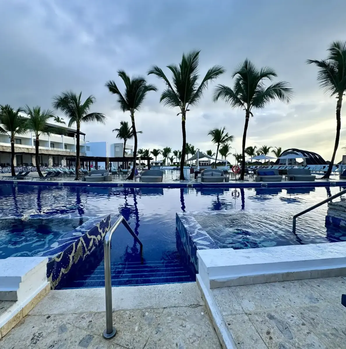Pool with steps, palm trees, and resort building in background
