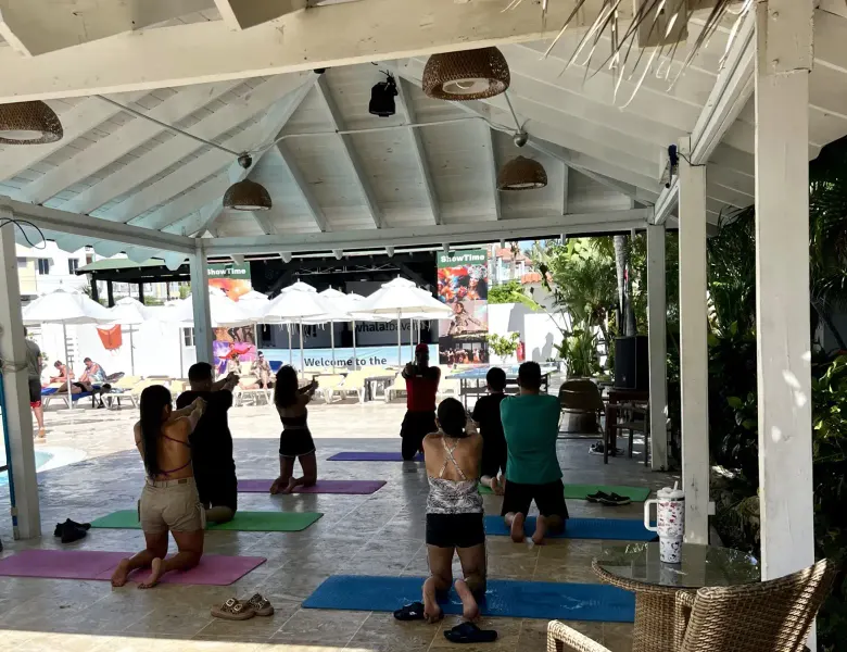 People doing yoga under a covered area near a pool with umbrellas