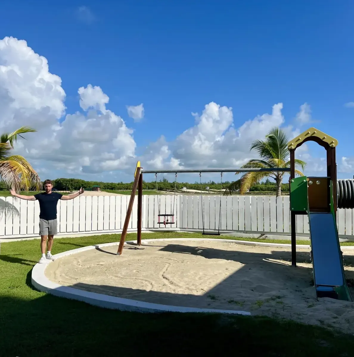 Man standing near playground with swings and slide on grass