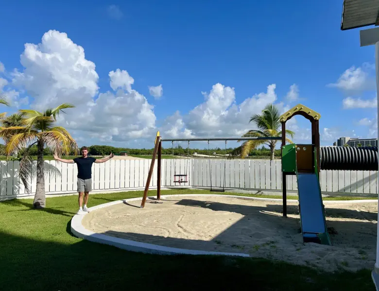 Man standing near playground with swings and slide on grass