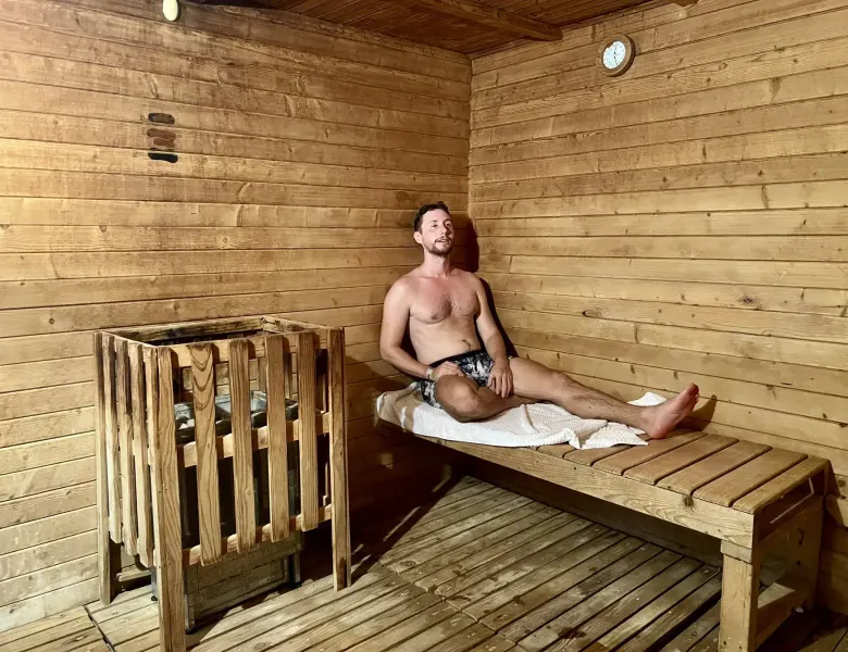 Man sitting on wooden bench in sauna with wood walls and heater